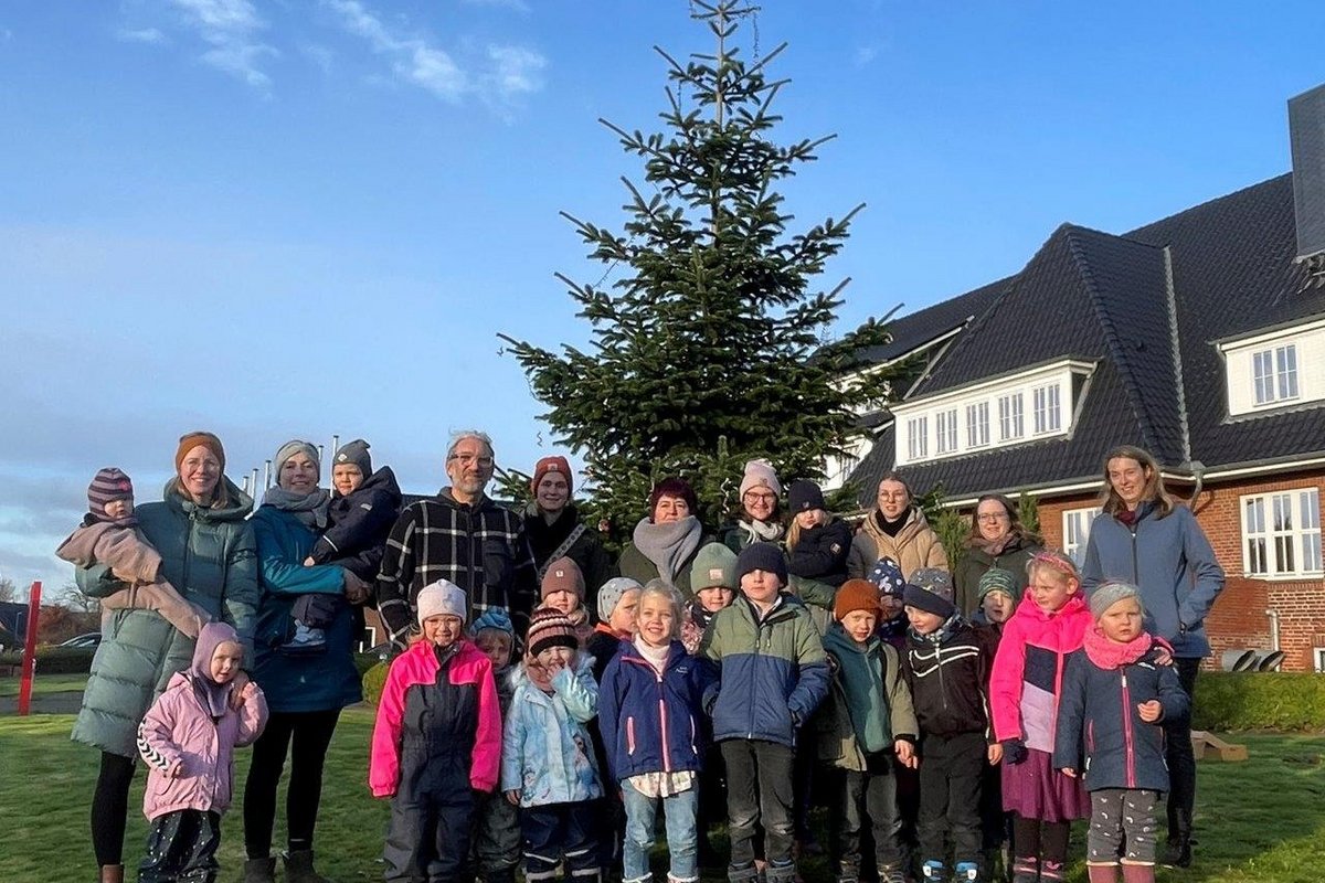 Viele kleine Kinder und einige Erwachsene stehen vor einem Tannenbaum