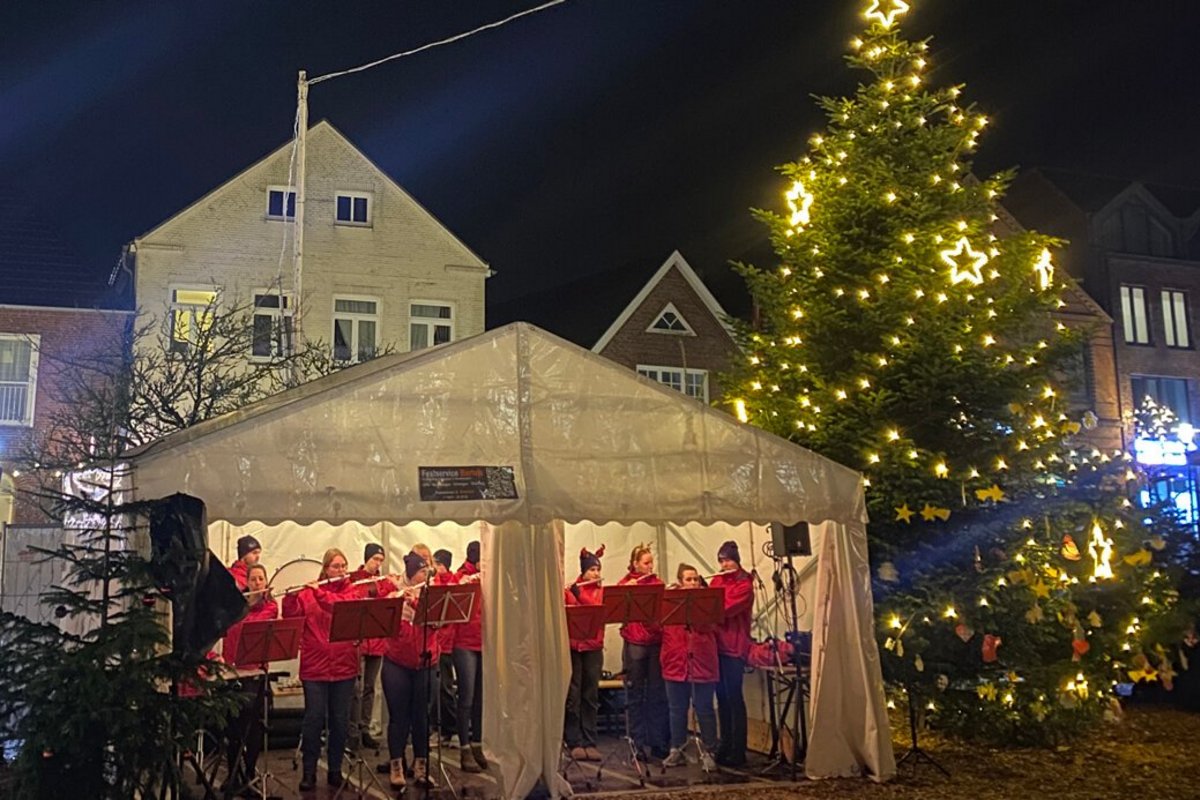 Neben einem haushohen Weihnachtsbaum stehen Musikanten in einem offenen Zelt. 